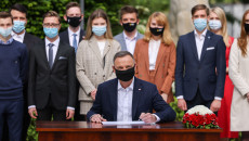 Prezydent RP Andrzej Duda podpisuje ustawę, za nim stoi grupa młodzieży