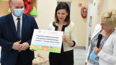 Uczestnicy otwarcia Klubu Seniora w Jędrzejowie. Kobieta trzyma kolorowy wydruk z napisem informującym szczegółach dofinansowania placówki