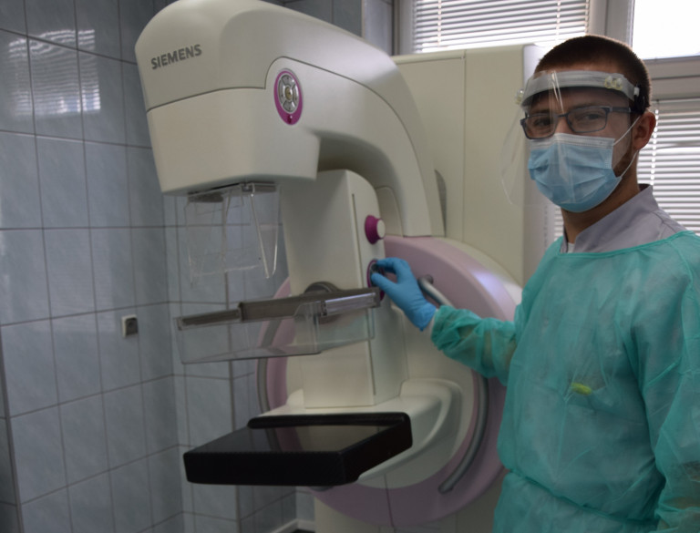 Lekarz ubrany w odzież ochronną stoi obok aparatury do mammografii