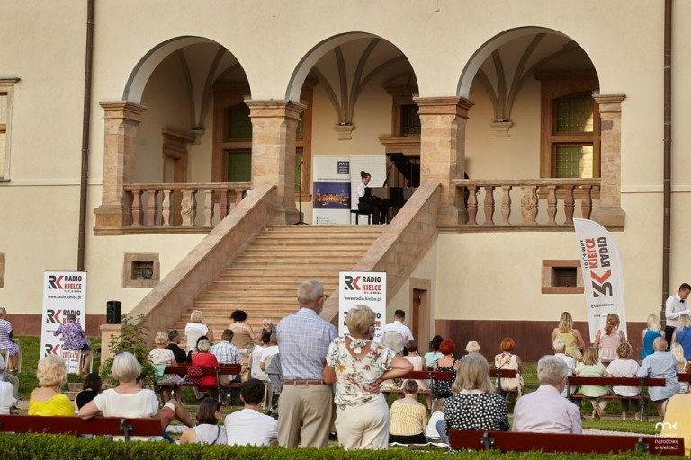 Publiczność zgromadzona w ogrodach muzeum narodowego w Kielcach słucha mężczyzny grającego na fortepianie