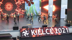 Na scenie tańczą ubrane na czarno dziewczynki. O scenę oparta szeroka plansza z napisem Kielce 2021. Festiwal harcerski w Amfiteatrze Kadzielnia
