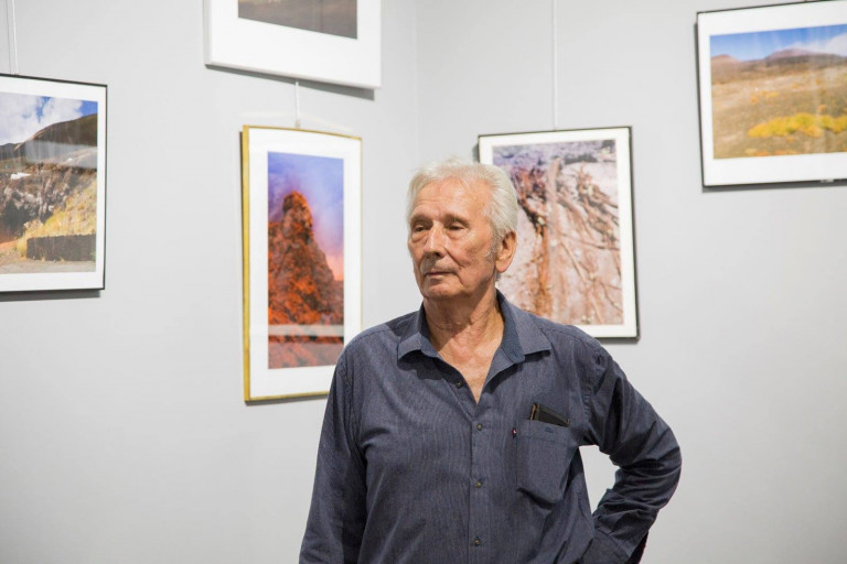 Henryk Pieczul oraz wiszące na ścianie za nim fotografie jego autorstwa