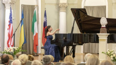 Koncert pianistki. Na scenie w sanatorium kobieta w niebieskiej sukni gra na fortepianie. Obok kobiety cztery flagi państw