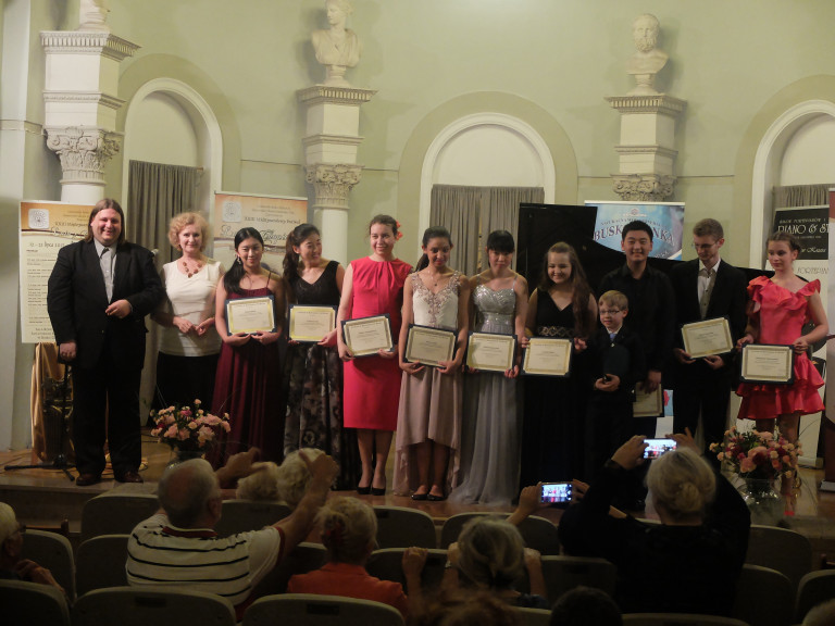Laureaci konkursu stoją na scenie, w rękach trzymają pamiątkowe dyplomy. Publiczność robi zdjęcia smartfonami