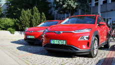 Dwa auta w kolorze czerwonym, z napędem elektrycznym stoją na parkingu przed głównym wejściem do siedziby urzędu marszałkowskiego