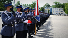 Na placu przed komendą, Policjanci stoją na baczność, salutują. Jeden z nich trzyma sztandar