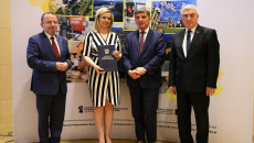 Uśmiechnięta urzędniczka z gminy Klimontów na fotografii z przedstawicielami samorządu województwa świętokrzyskiego, prezentuje okolicznościowy dyplom