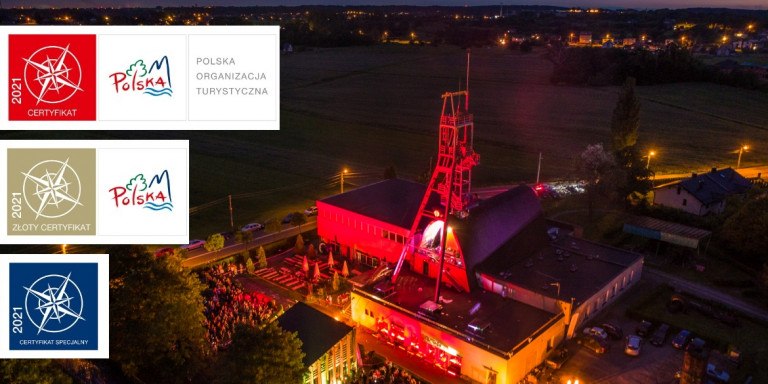 Kompleks niskich budynków oświetlonych nocą czerwonym światłem. Na dachu budynku metalowa konstrukcja przypominająca mały taras widokowy. Certyfikat Polskiej Organizacji Turystycznej 2021t