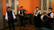 Kapela Ludowa Bliżej Serca. Czterech mężczyzn ubranych w stroje ludowe gra na instrumentach muzycznych w rogu sali lustrzanej