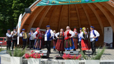 Na scenie w parku grupa osób w kolorowych strojach tańczy podśpiewując ludowe pieśni