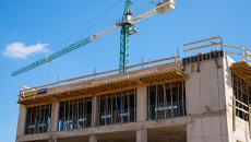 Zdjęcie zbliżenie na ostatni poziom konstrukcji budynku w stanie surowym na placu budowy. Zza budynku wystaje wysoki dźwig w kolorze zielonym