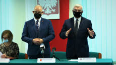 Za stołem stoi dwóch mężczyzn w maseczkach ochronnych. Pierwszy z prawej to marszałek Andrzej Bętkowski, mówi do zgromadzonych o konieczności Inwestowania w proekologiczne działania