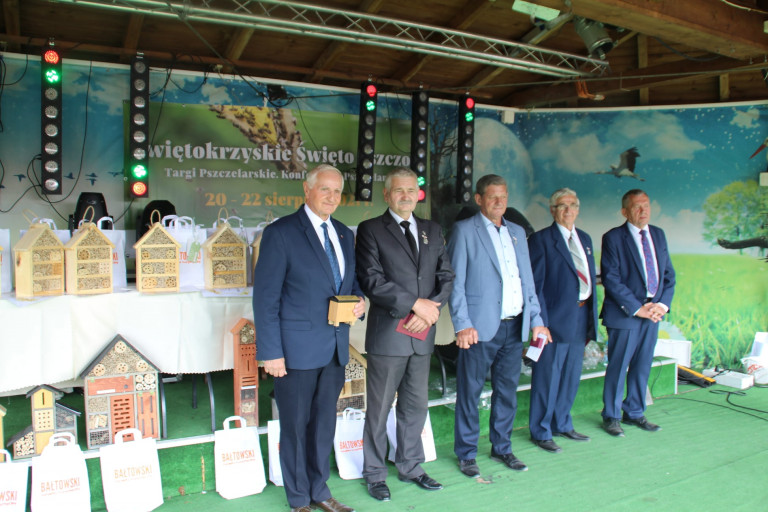 Członek Zarządu Województwa Świętokrzyskiego Marek Jońca Na Scenie, Obok Stoją Mężczyżni W Garniturach