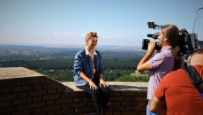 Prowadząca program pozuje do pamiątkowego zdjęcia na wieży Zamku w Chęcinach. Za kobietą linka ochronna. W tle panorama gór świętokrzyskich w słoneczny dzień