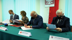 Grupa osób siedzi za stołem. Urzędnicy podpisują dokumenty.