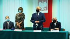 Za stołem grupa osób. Stoją kobieta i mężczyzna. Za nimi na ścianie godło Polski. Pierwszy z prawej to Andrzej Bętkowski, marszałek województwa