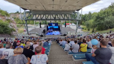 Szerokie zdjęcie. Widok na scenę z górnych rzędów amfiteatru na Kadzielni. Siedząca publiczność ogląda koncert