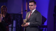 Młody mężczyzna w okularach, Laureat trzyma statuetkę i przemawia do mikrofonu