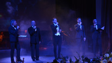 Pięciu mężczyzn w ciemnych garniturach śpiewa na scenie