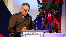Mężczyzna w mundurze przemawia, w tle stoją statuetki nagrody i czerwone róże