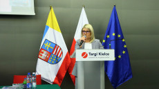 Dyrektor Katarzyna Kubicka mówi do mikrofonu na tle flag.