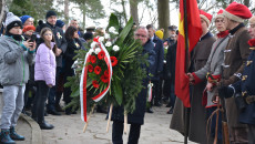 Marek Bogusławski idzie z wiążanką kwiatów, by ją złożyć na pomniku