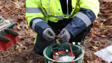 Mężczyzna W Zielonej, Odblaskowej Kurtce Skręca Przewwody Elektryczne W Studzience Ziemnej