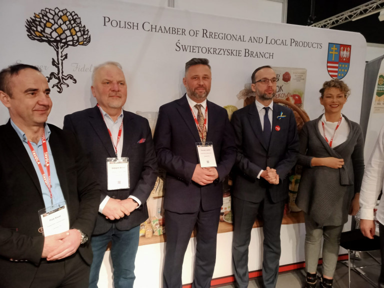 Piotr Kisiel, Grzegorz Banaś, Tomasz Jamka oraz mężczyzna i kobieta stoją w hali targowej