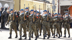 Grupa żołnierzy w mundurach i niebieskich beretach maszeruje na rynku