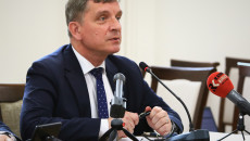 Andrzej Pruś Siedząc Za Stołem Przemawia Do Mikrofonu