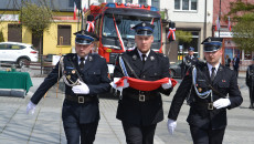 Strażacy w mundurach niosą złożoną flagę państwową