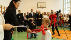 Dyrektor w czerni pasuje chłopca na ucznia czerwonym ołówkiem