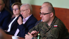 Mężczyzna w wojskowym mundurze, obok niego inny mężczyzna i kobieta siedzą za stołem