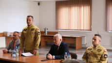 Komendant straży pożarnej w Skrażysku stoi przy stole w żółtym umundorowaniu