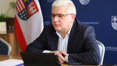 Andrzej Swajda siedzi na tle flagi województwa.