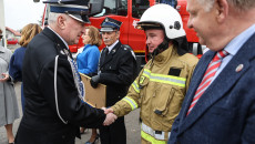 Marszałek Andrzej Bętkowski podaje dłoń strażakowi. W tle samochód strażacki oraz strażacy