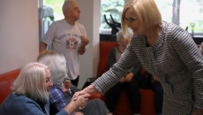 W pomieszczeniu grupa starszych osób. Uśmiechnięta Wicemarszałek Renata Janik wita się ze starszą kobietą podając jej dłoń.