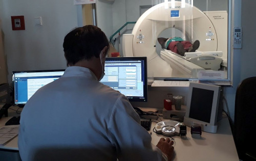 Lekarz Siedzi Przed Monitorem Komputera, W Tle Pacjent Poddawany Badaniu Tomograficznemu