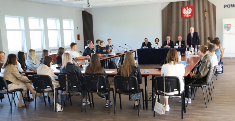 Uczestnicy Spotkania Siedzą Za Stołami Słuchają Przemówienia