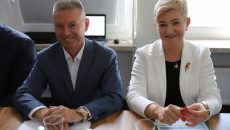 Kobieta W Białym żakiecie Oraz Mężczyzna W Niebieskiej Marynarce Siedzą Przy Stole W Sali Obrad